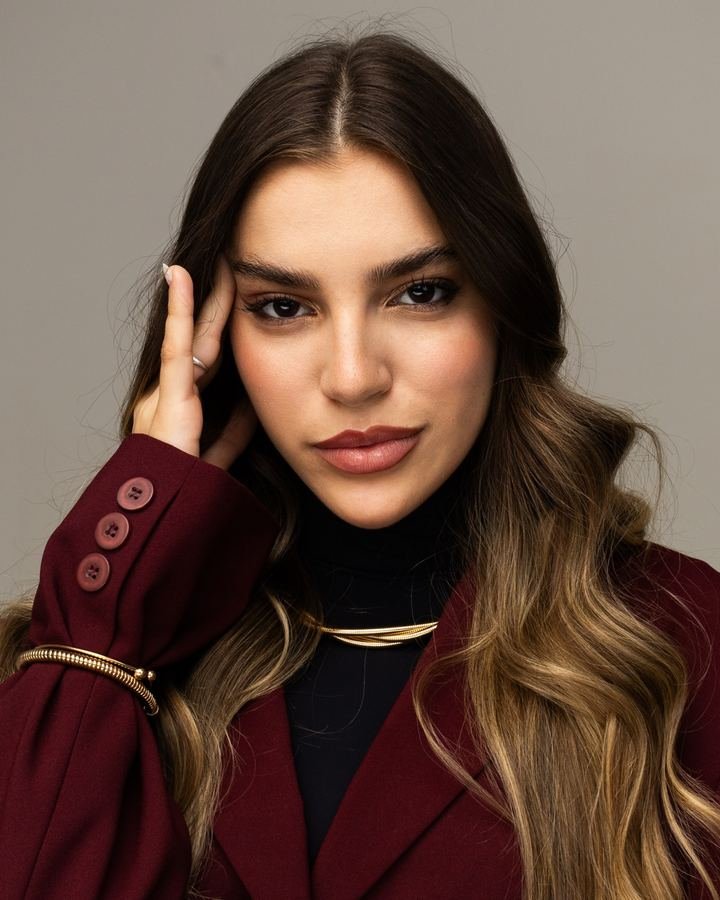 Dra.&nbsp;Isa Folador de blazer vinho, com a mão no rosto, olhando para a câmera